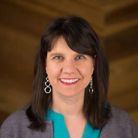 Head shot of Janet wearing a gray sweater over a teal blouse with silver earrings